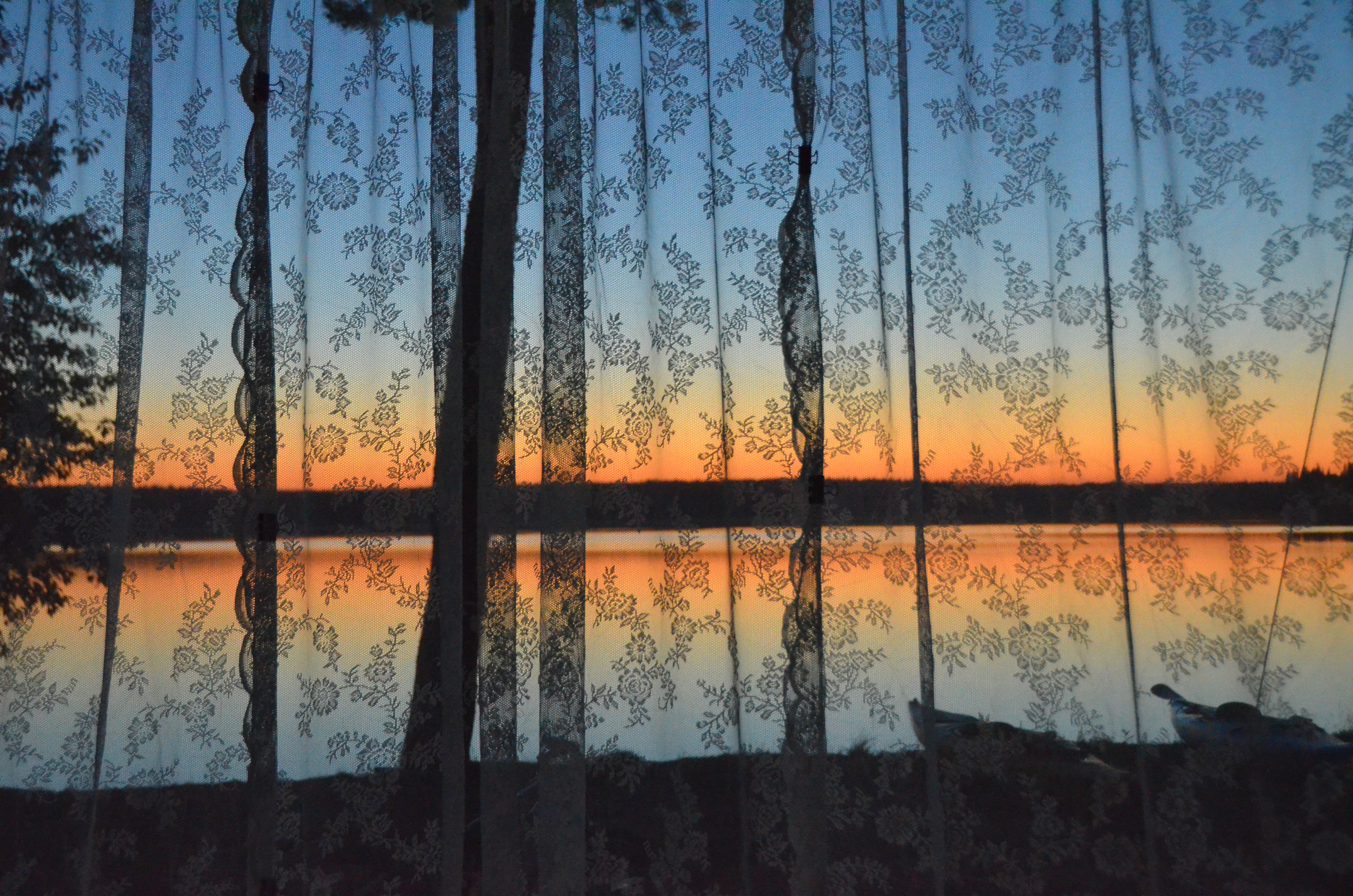 Looking through the lace curtains to a brilliant orange sunset that is reflected in the still waters of One Island Lake.