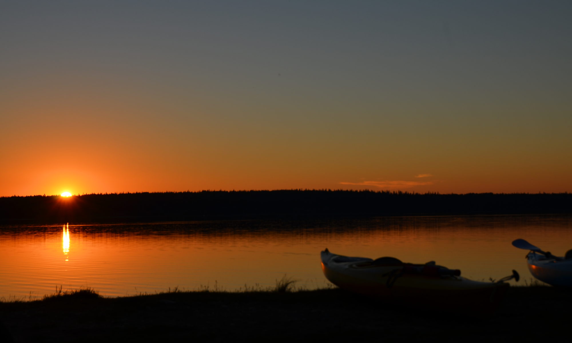The setting sun reflected in a lake with kayaks in the foreground