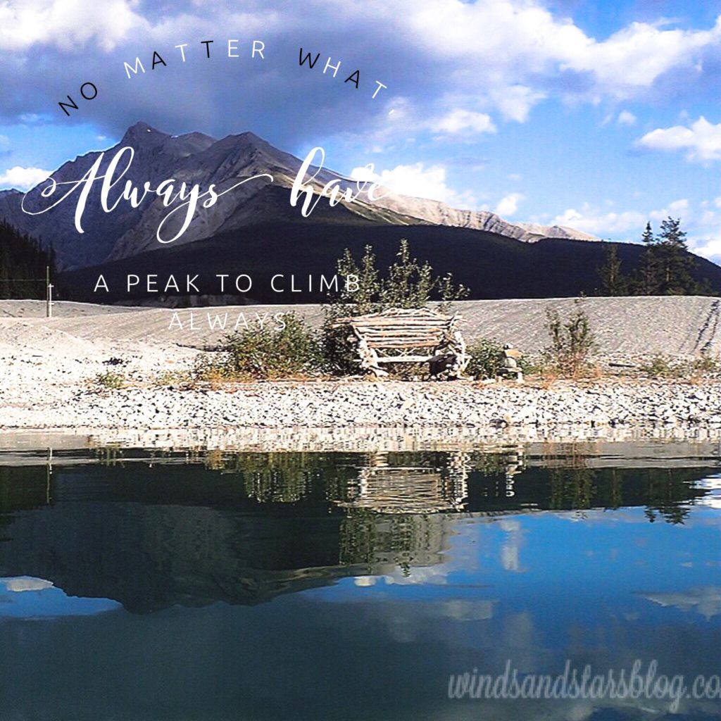 The mountains reflected in the water with a bench crafted with sticks is at the water edge.  The sky is blue but partially cloudy.  The words, "no matter what, always have a peak to climb" is written across the picture. Without dreams we lose purpose.