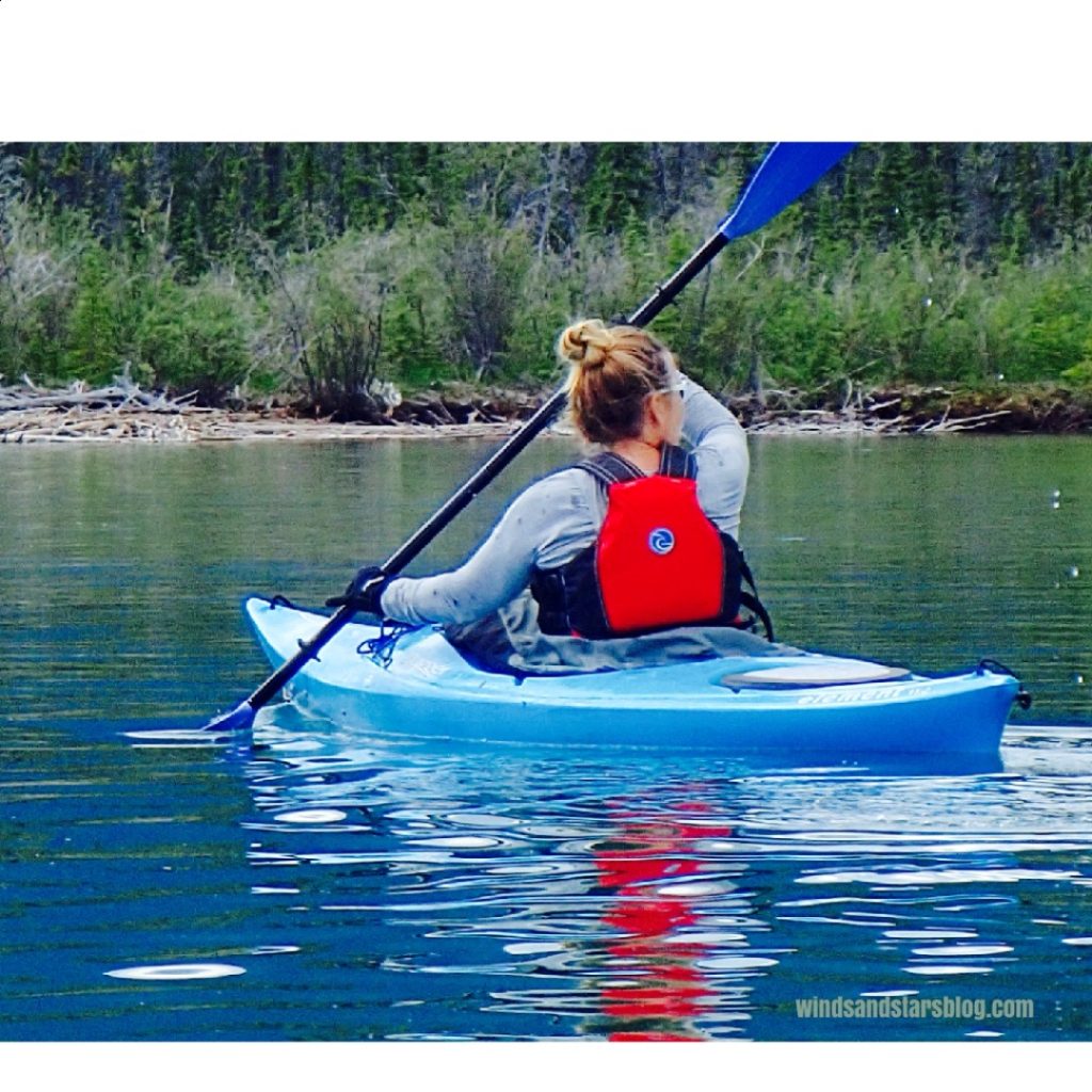 A backview of me paddling a blue kayak on a lake.