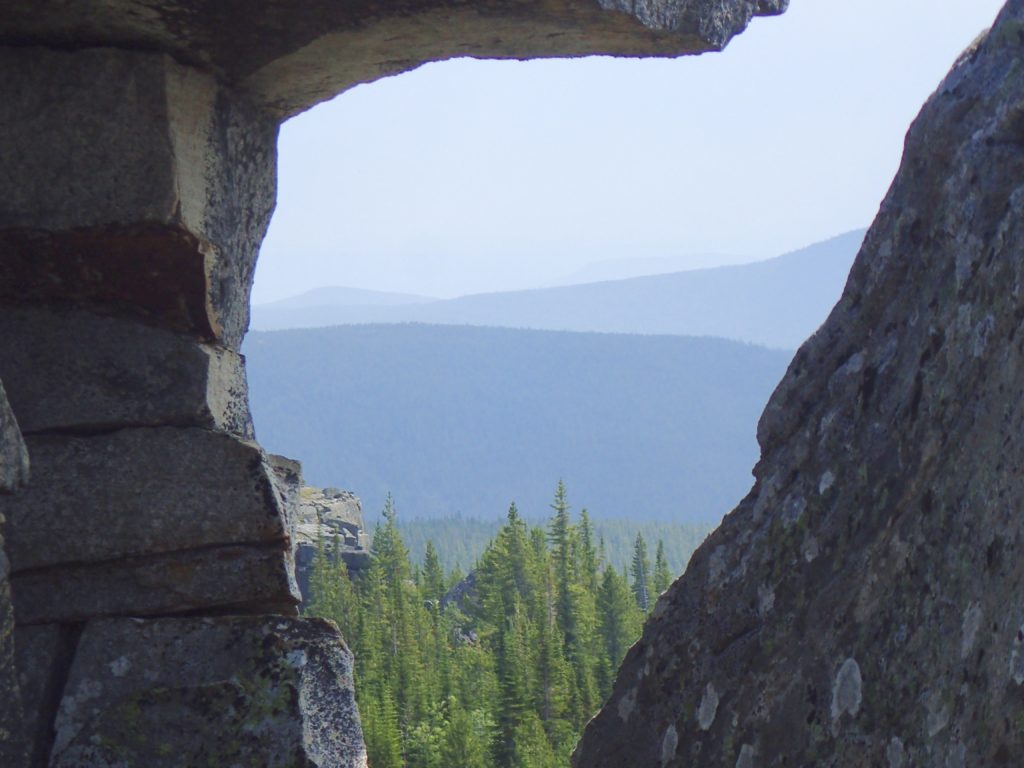 a triangular shaped 'window' in a rock face show evergreen trees in the foreground and blue mountain ranges in the background. Dreams are windows filled with possibility.